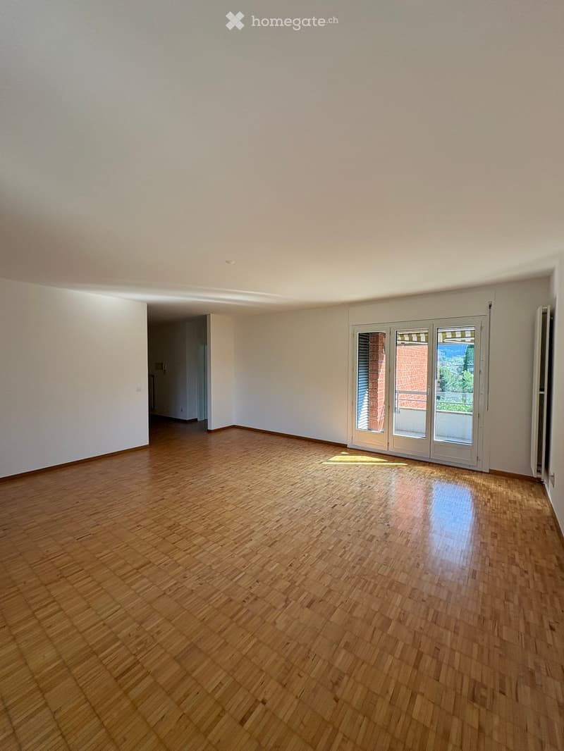 Empty room with wooden flooring and white walls, featuring a large sliding glass door leading to a balcony.