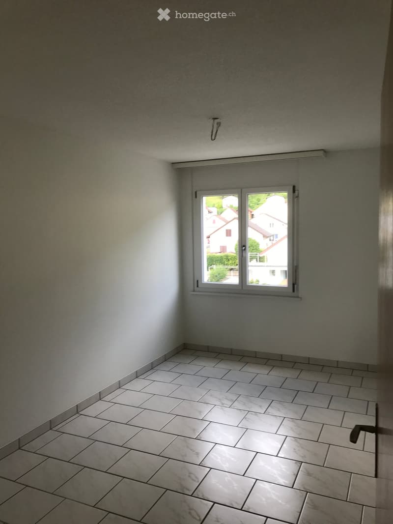 Empty room with tiled floor and white walls, featuring a window with a view of neighboring houses.
