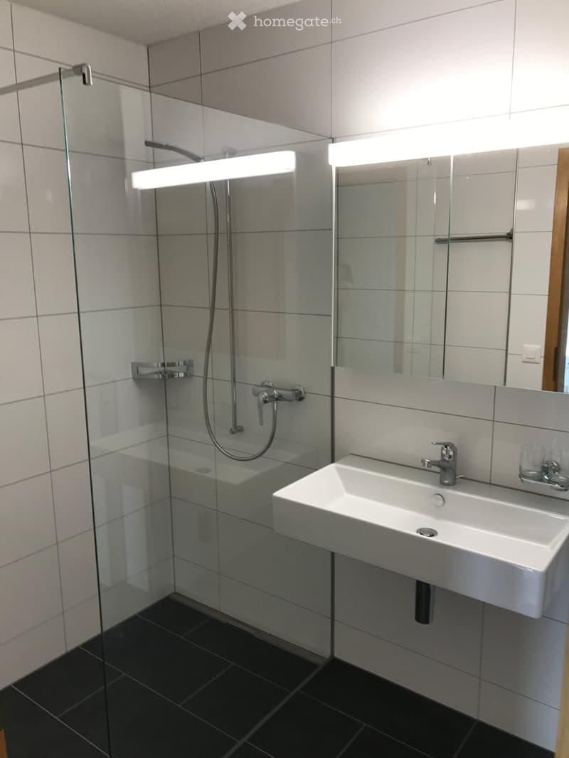 Modern bathroom with white tiles, a glass-enclosed shower, a white sink with a modern faucet, and a large mirror with built-in lighting.