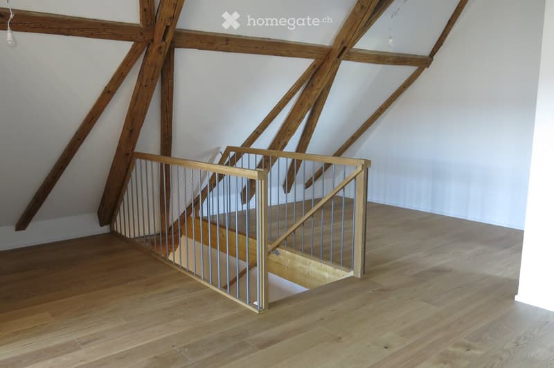 Spacious hallway with wooden floors, exposed wooden beams, and a modern staircase with a metal railing leading upwards.