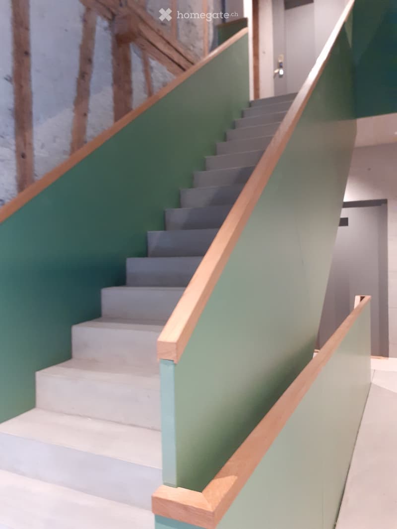 Staircase with grey steps and wooden handrails, green walls, modern design.