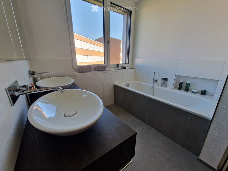 Modern bathroom with two sinks, a bathtub, and a window with a view of the building exterior.