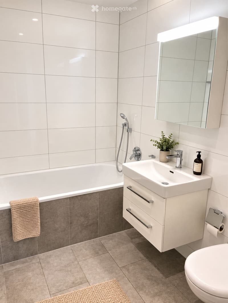 Modern bathroom with a white tiled wall, a bathtub, a sink with a modern faucet, a large mirror, a towel, a toilet, and a small plant on the sink counter.