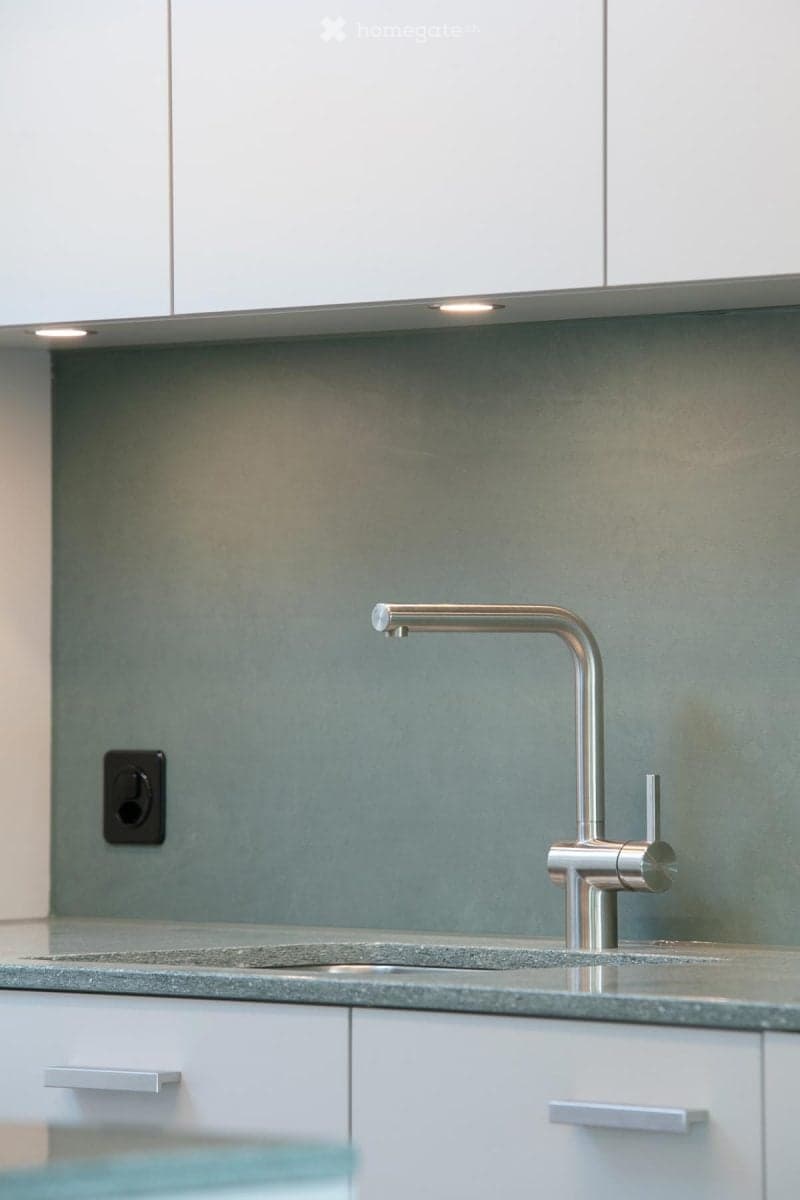 Modern kitchen with a sleek, stainless steel faucet, a grey countertop, and white cabinets.