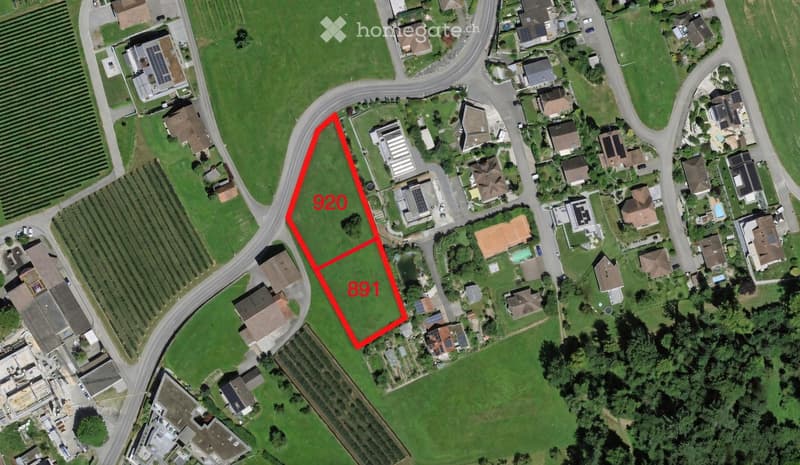 Aerial view of a residential area with multiple houses, green spaces, and a highlighted plot marked with the numbers 920 and 891.