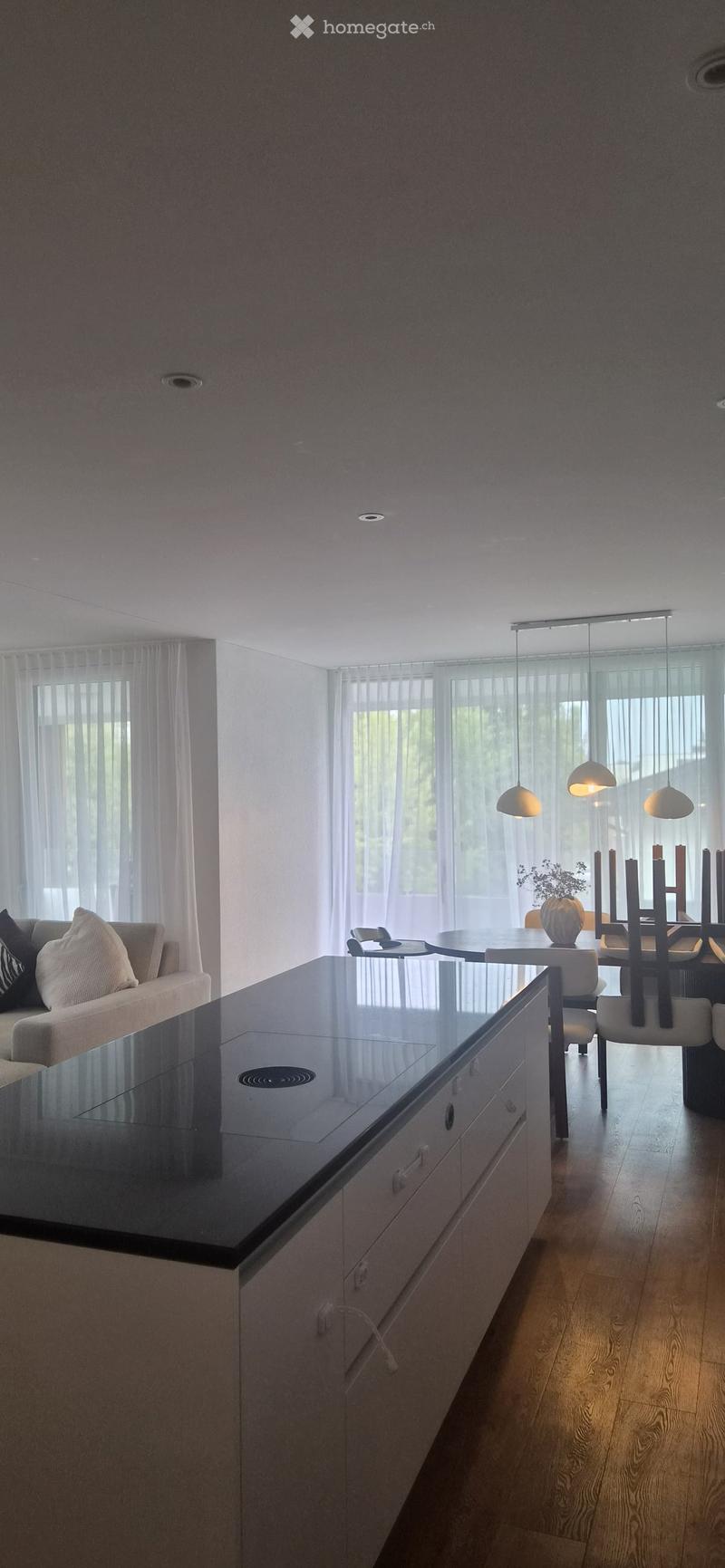 Modern open-plan living and dining area with a sleek black countertop, white cabinets, a grey sofa, and a dining table with chairs.