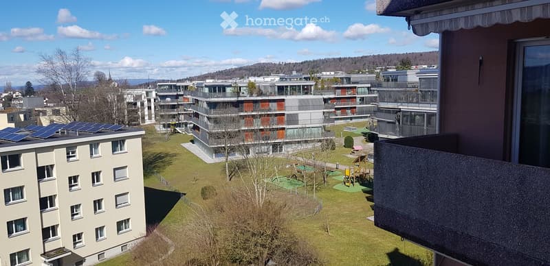 View of a residential complex with modern apartment buildings, solar panels on rooftops, and a green courtyard with playground equipment.