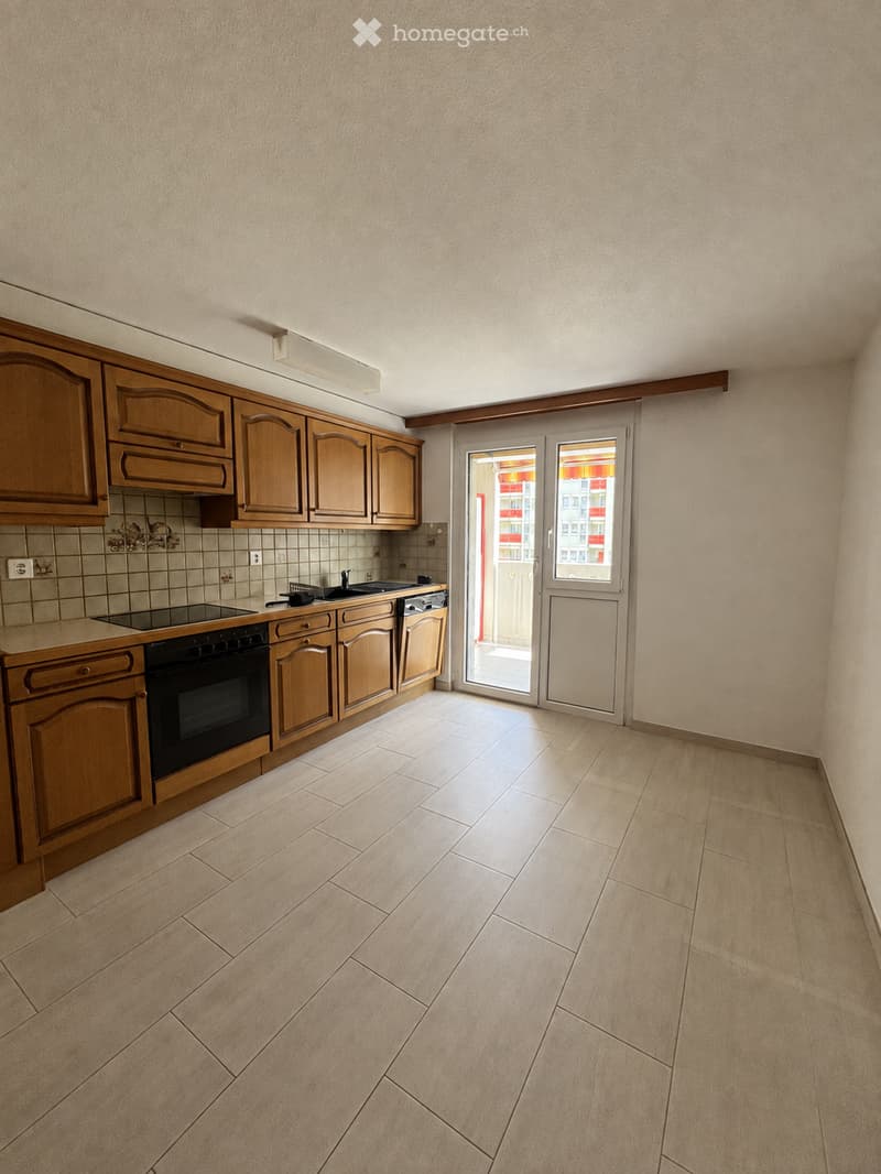 Empty kitchen with light wooden cabinets, a built-in oven, a sink, and a tiled backsplash. The floor is tiled, and there is a sliding glass door leading to a balcony.