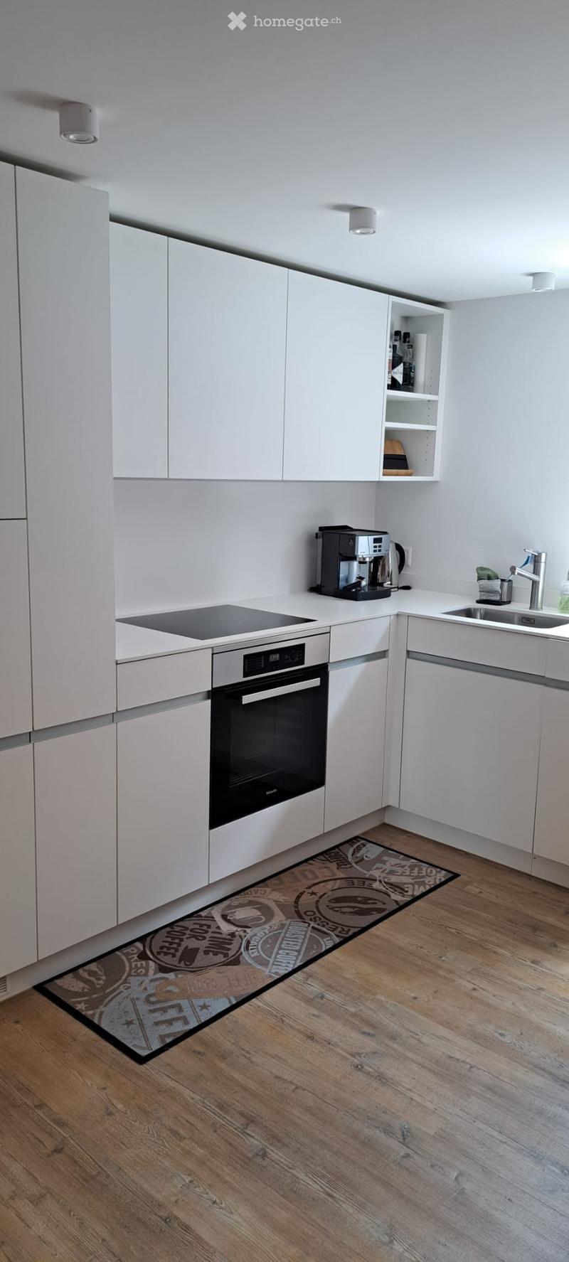 Modern kitchen with white cabinets, wooden flooring, and stainless steel appliances including an oven, coffee maker, and sink.