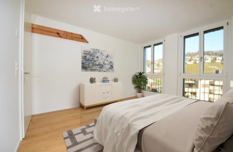 Modern bedroom with wooden flooring, large windows offering a view, a neatly made bed, a nightstand, a white cabinet, a potted plant, and a piece of abstract artwork on the wall.