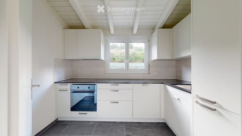 Modern kitchen with white cabinets, a built-in oven, and a black countertop. The space features large windows and a sleek, minimalist design.