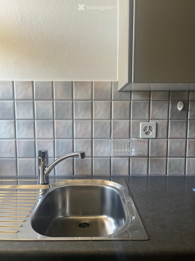 Modern kitchen sink with a stainless steel faucet, a single-basin sink, and a small glass cup on the counter.