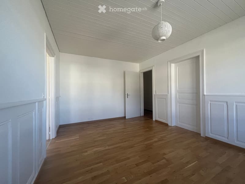 Empty hallway with wooden flooring, white walls, and several doors leading to other rooms.