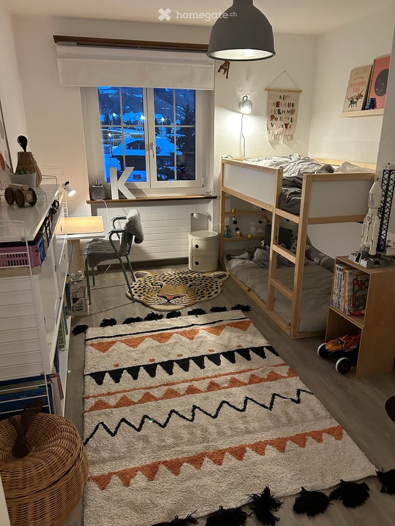 Cozy bedroom with bunk bed, colorful rug, wicker basket, and various toys and books.