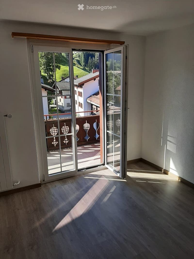 Empty room with wooden flooring and large sliding glass doors leading to a balcony with a scenic view of the countryside.