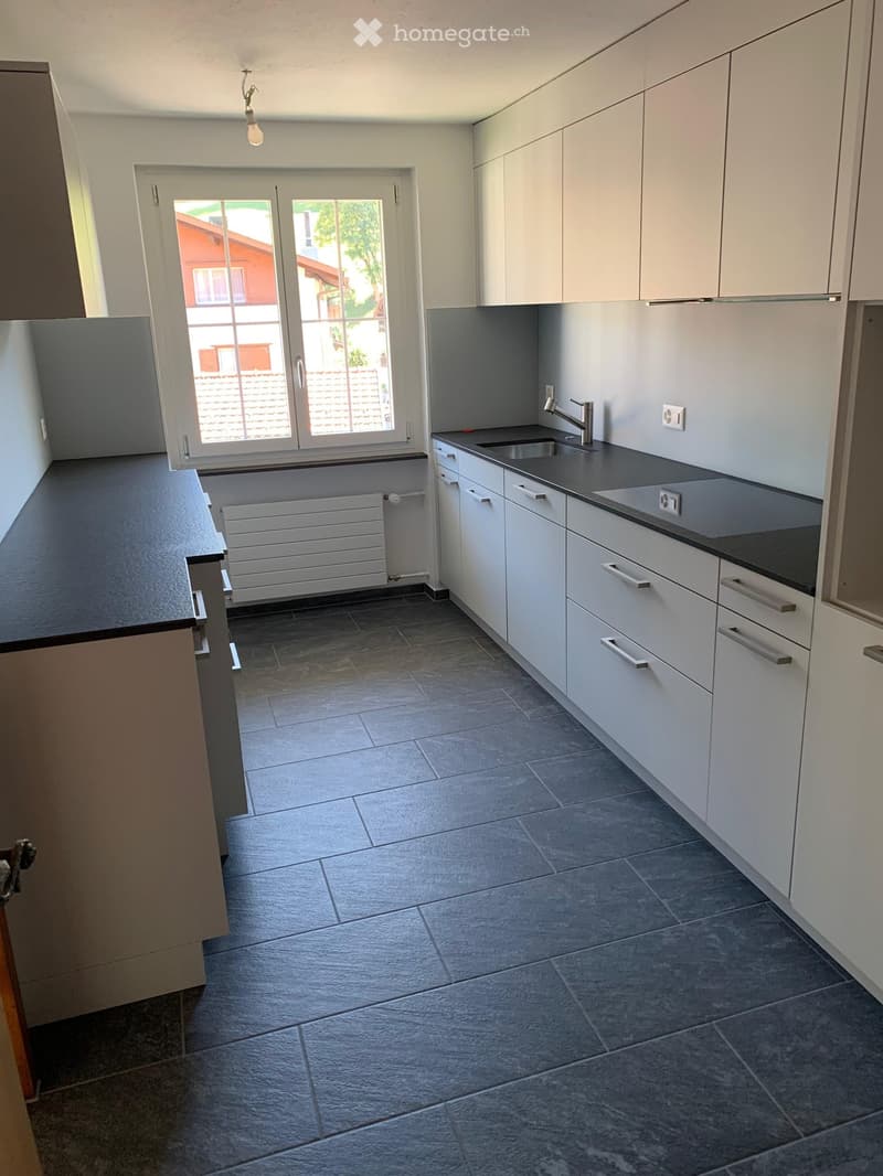 Modern kitchen with white cabinets, dark countertops, and tiled floor. Features a sink, faucet, and radiator.
