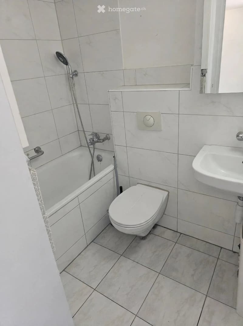 Modern bathroom with white tiles, a bathtub, toilet, sink, and a showerhead.