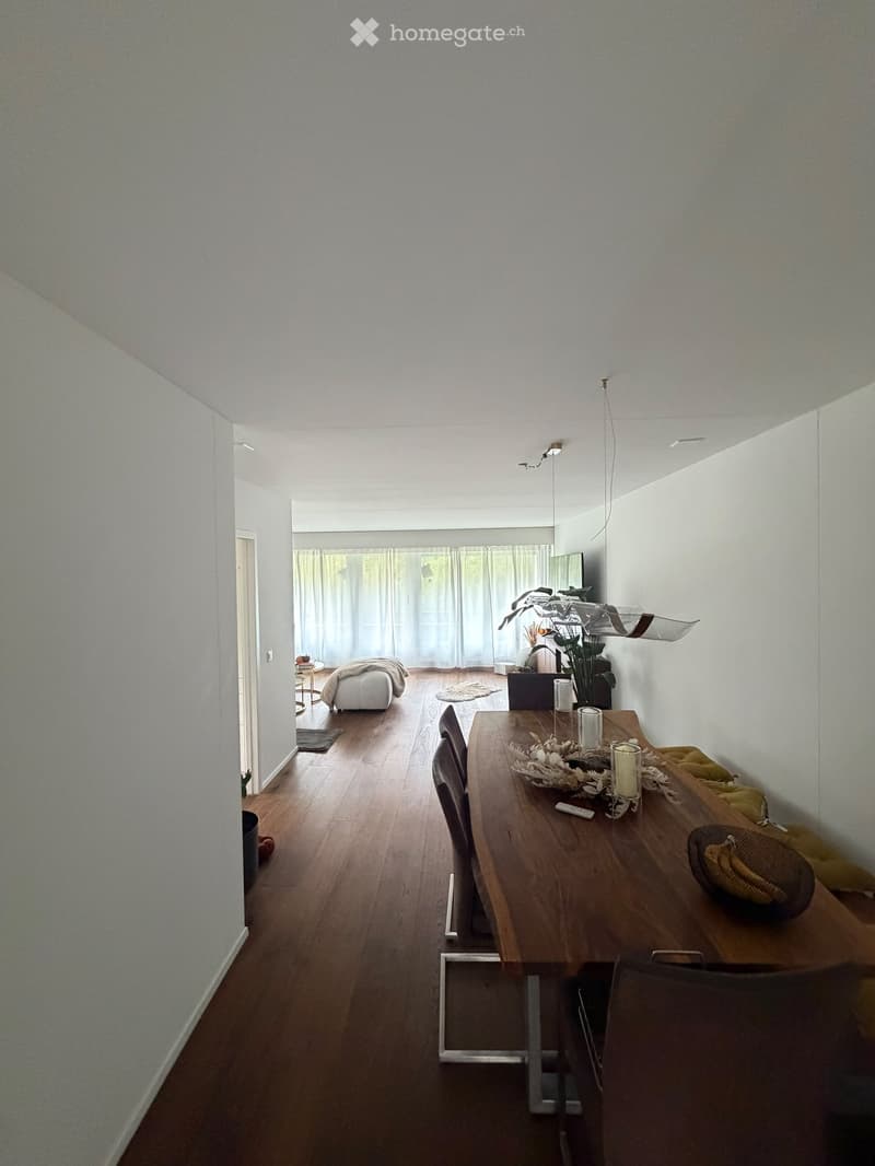 Open-plan living and dining area with wooden flooring, white walls, and modern decor including a dining table, chairs, a sofa, and decorative items.