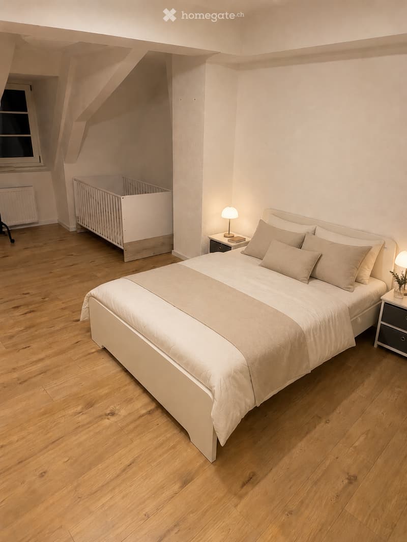 Cozy bedroom with wooden flooring, a large bed with beige bedding, a nightstand with a lamp, a small cradle, and a radiator near the window.