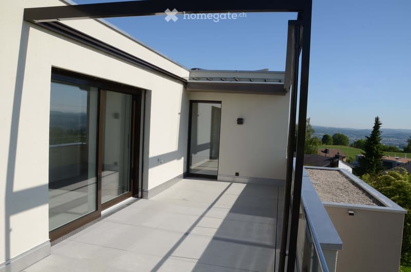 Modern balcony with large glass doors, tiled floor, and a view of the surrounding landscape.