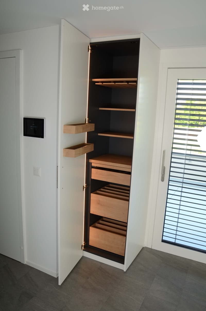 An empty room with a built-in storage unit featuring wooden shelves and drawers, white walls, and a large window with blinds.