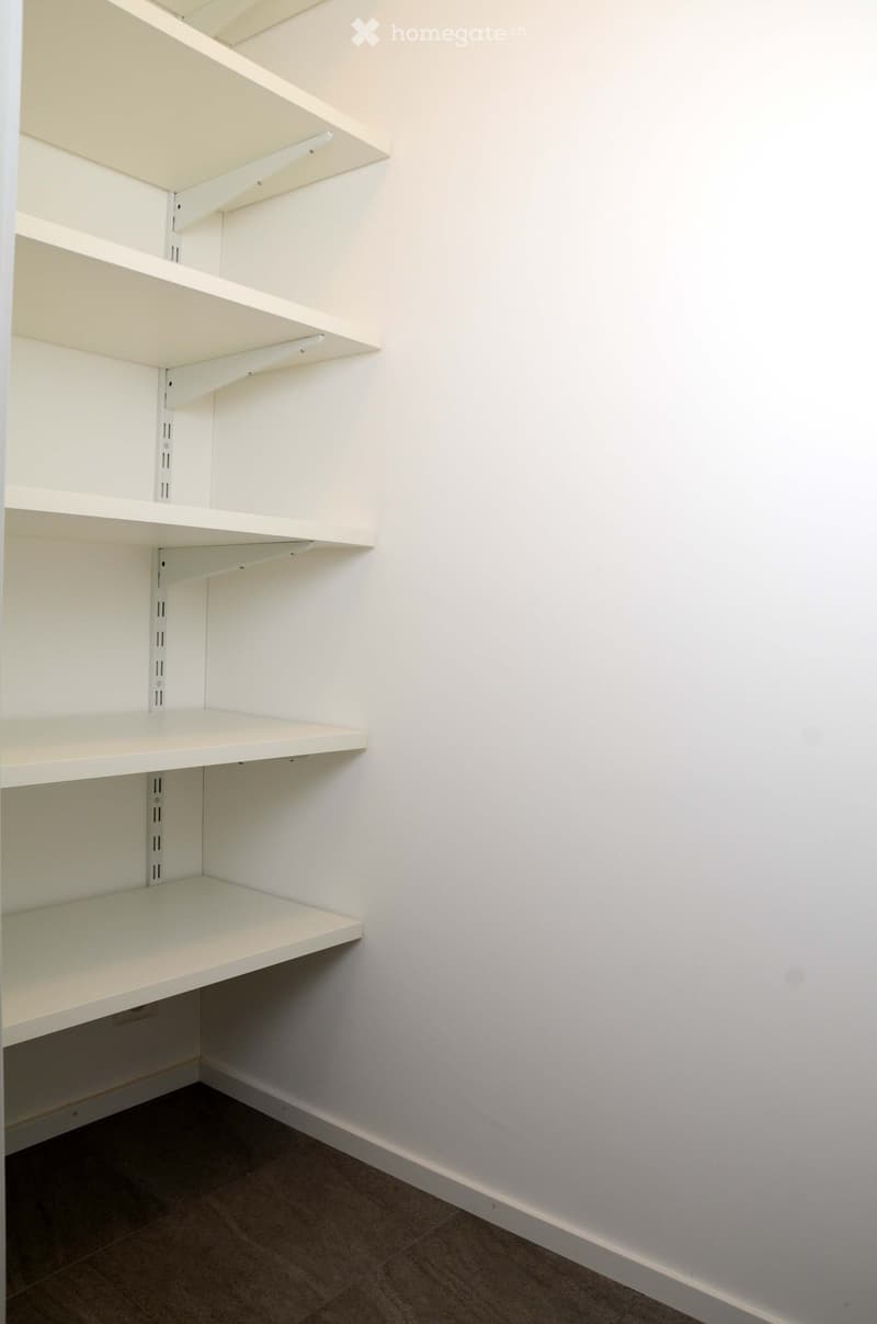 Empty closet with white, adjustable shelves and built-in lighting, featuring a clean, minimalist design with a tiled floor.