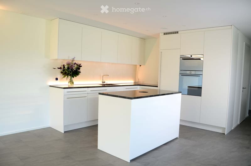 Modern kitchen with white cabinets, black countertops, and built-in appliances. Features a central island, sink, and decorative vase with flowers.