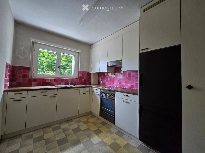 Bright kitchen with white cabinets, a stainless steel oven, a refrigerator, and a sink. The walls are adorned with pink tiles, and the floor features a checkered pattern.