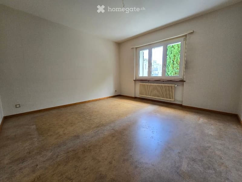 Empty room with beige carpet, light-colored walls, and a large window with a radiator below it.
