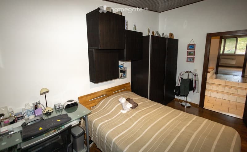 A well-furnished bedroom with a bed, desk, wardrobe, and mirror. The room features a wooden floor and white walls.