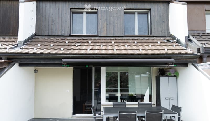 Outdoor patio area with a table and chairs, large glass sliding doors leading inside, and a covered awning above.