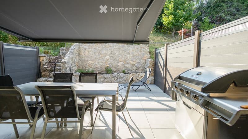 Outdoor patio with a covered area, a stone wall backdrop, a dining table with chairs, and a modern grill.