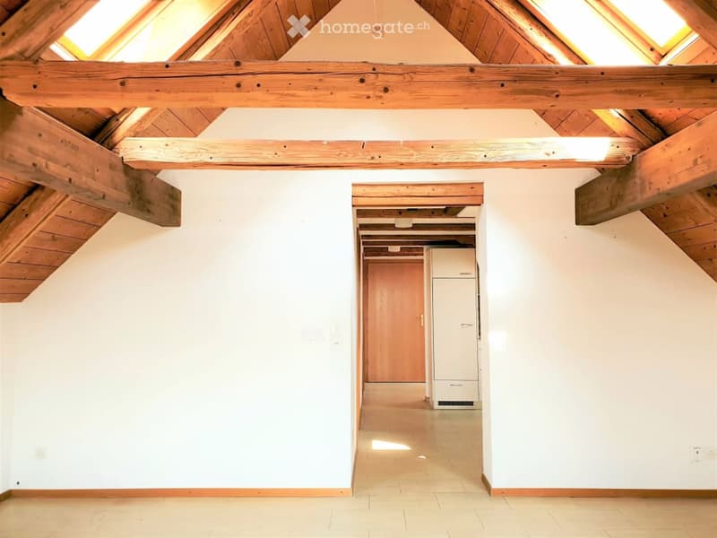 Empty attic space with wooden beams, white walls, and a tiled floor. No furniture or equipment present.