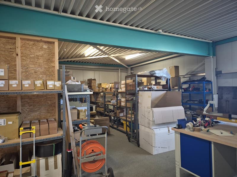 Other. A spacious storage or workshop area with metal shelving units filled with cardboard boxes, a workbench with tools, and a handcart with coiled orange hose.