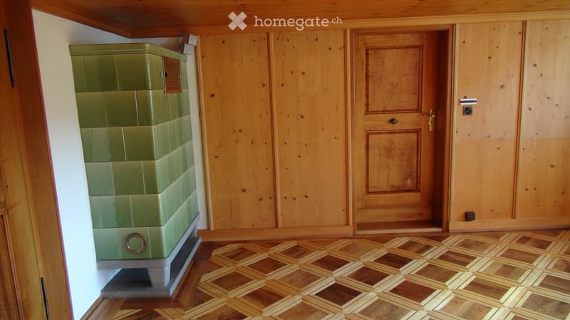 Empty room with wooden walls, wooden floor, and a green tiled stove. No furniture or equipment present.