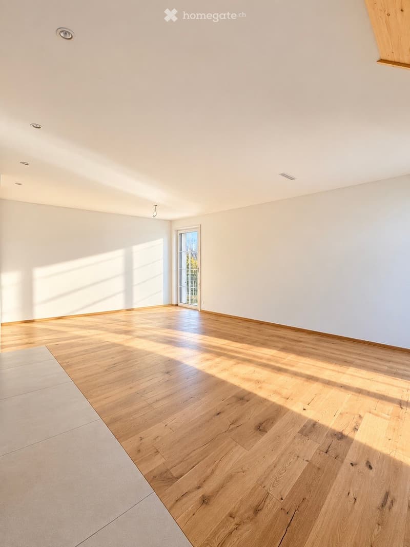 Empty room with light wooden flooring and white walls, featuring a large window allowing natural light to enter.
