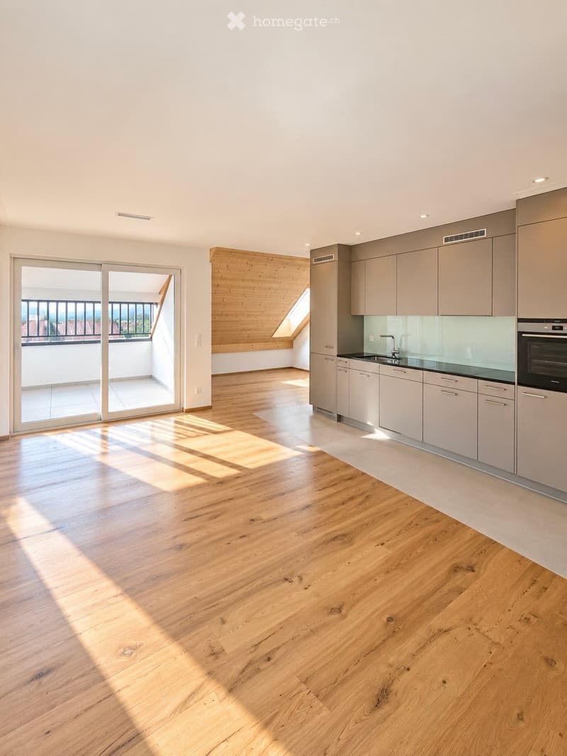 Open-plan space with light wooden flooring, modern kitchen cabinets, and a sliding glass door leading to a balcony.