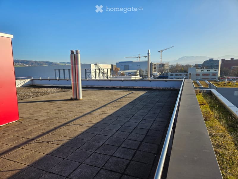 Roof terrace with tiled surface, metal railing, and distant cityscape view.