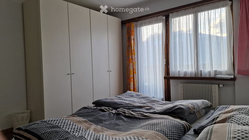 Bedroom with a double bed, patterned bedding, large wardrobe, window with curtains, radiator, and a small basket on the floor.