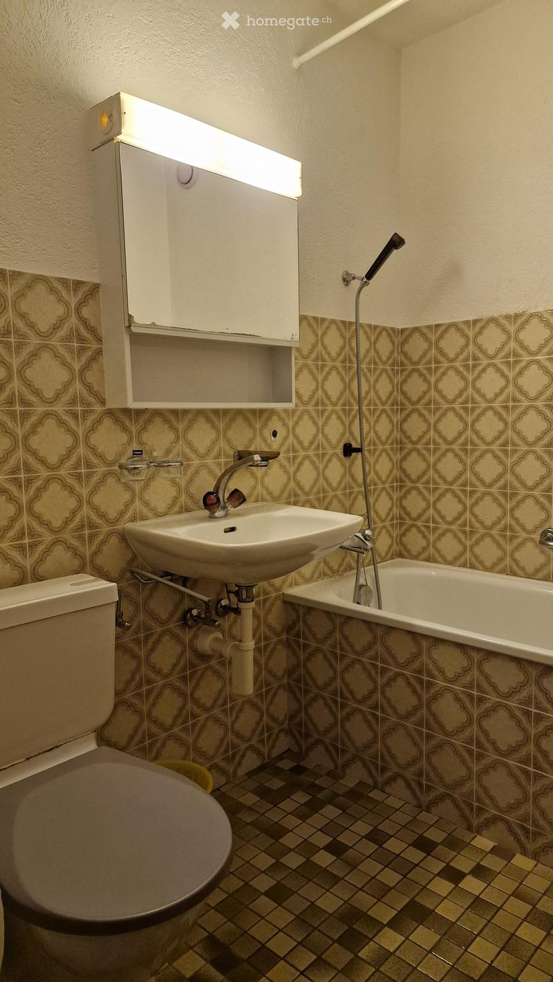 Bathroom with a toilet, sink, bathtub, and medicine cabinet. The walls are tiled with a floral pattern, and the floor has a checkered tile design.