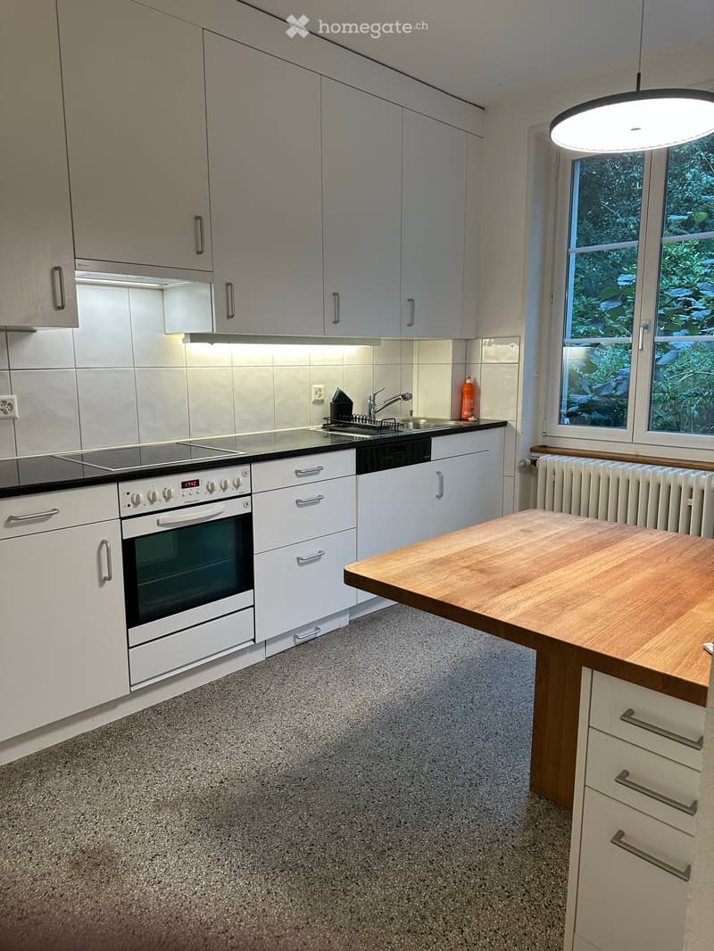 Modern kitchen with white cabinets, stainless steel appliances, and a wooden countertop.
