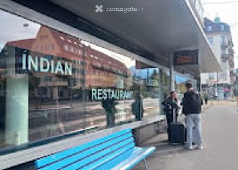 A public sidewalk with a blue bench, a restaurant sign reading "INDIAN RESTAURANT" visible in the background, and a few pedestrians.