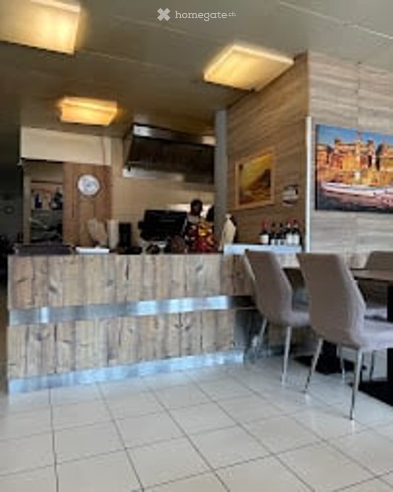 Modern interior with a wooden counter, seating area with chairs and a table, and a framed picture on the wall.