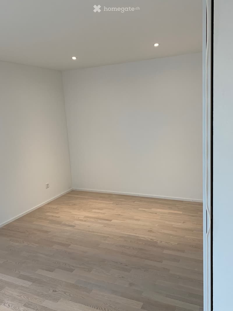 Empty room with hardwood floors, white walls, and ceiling lights