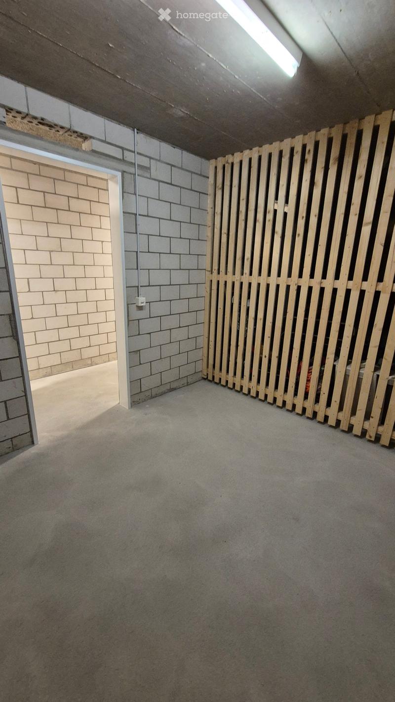 Empty room with concrete floor, exposed brick walls, and a wooden barrier on one side.