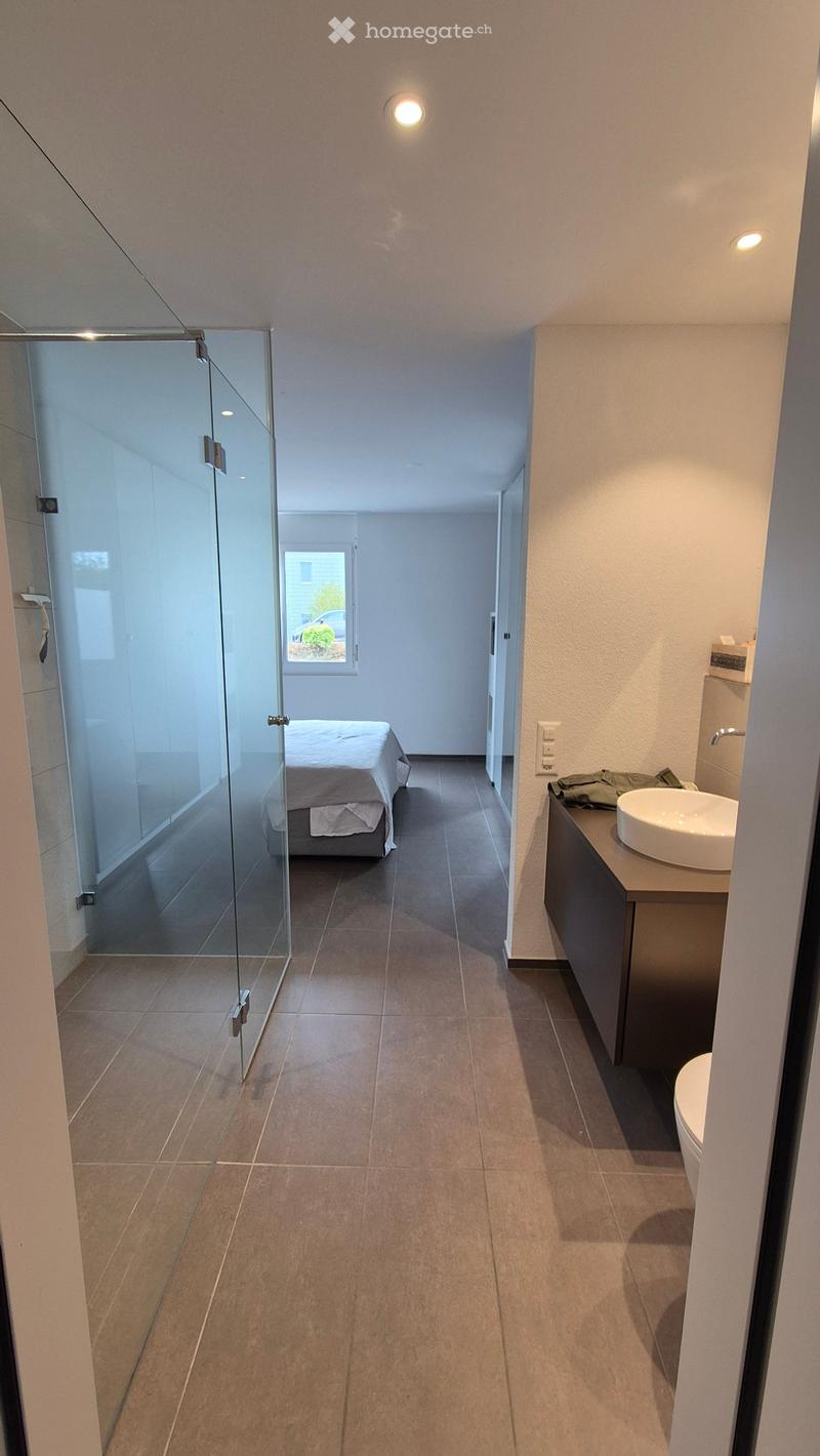 Modern hallway leading to a bedroom and bathroom area with a sink, toilet, and cabinet.