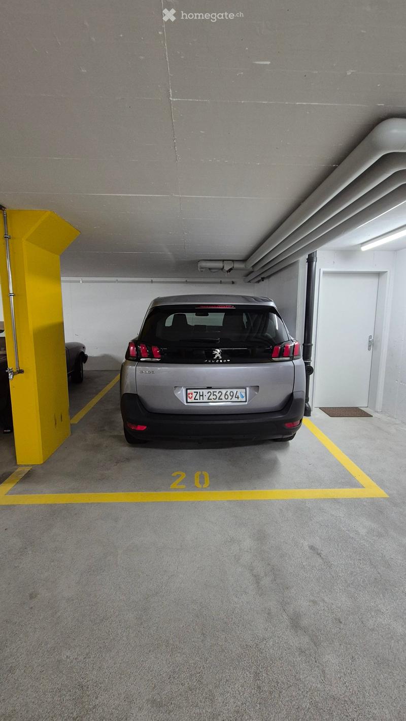 Underground parking space with a single car parked in bay number 20, marked with yellow lines and a yellow pillar.
