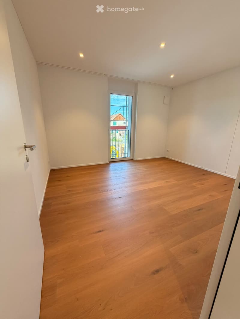 Empty room with light wooden flooring, white walls, and a sliding glass door leading to a balcony.