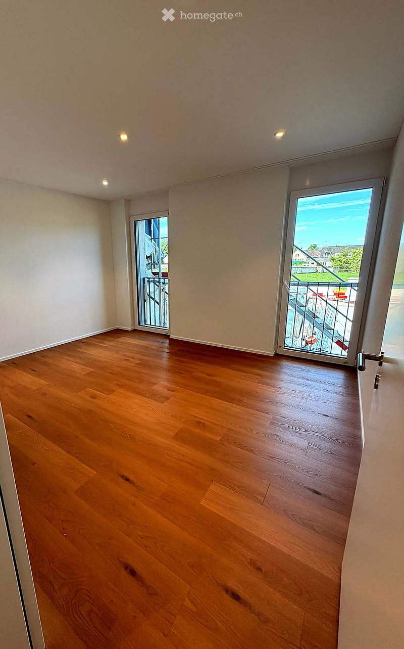Empty room with wooden flooring, white walls, and two sliding glass doors leading to a balcony.