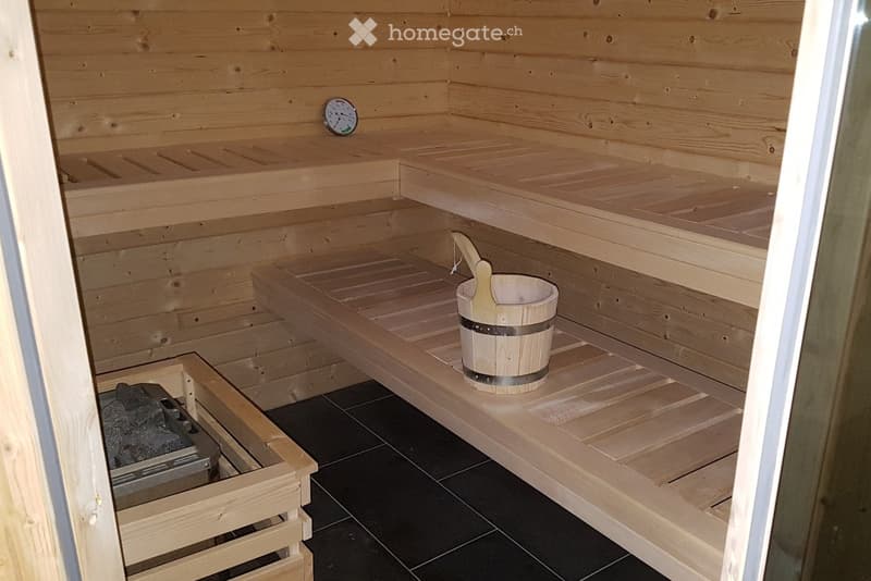 a wooden sauna with a small clock on the wall, a bucket with a ladle, 2 benches, and a stone bin